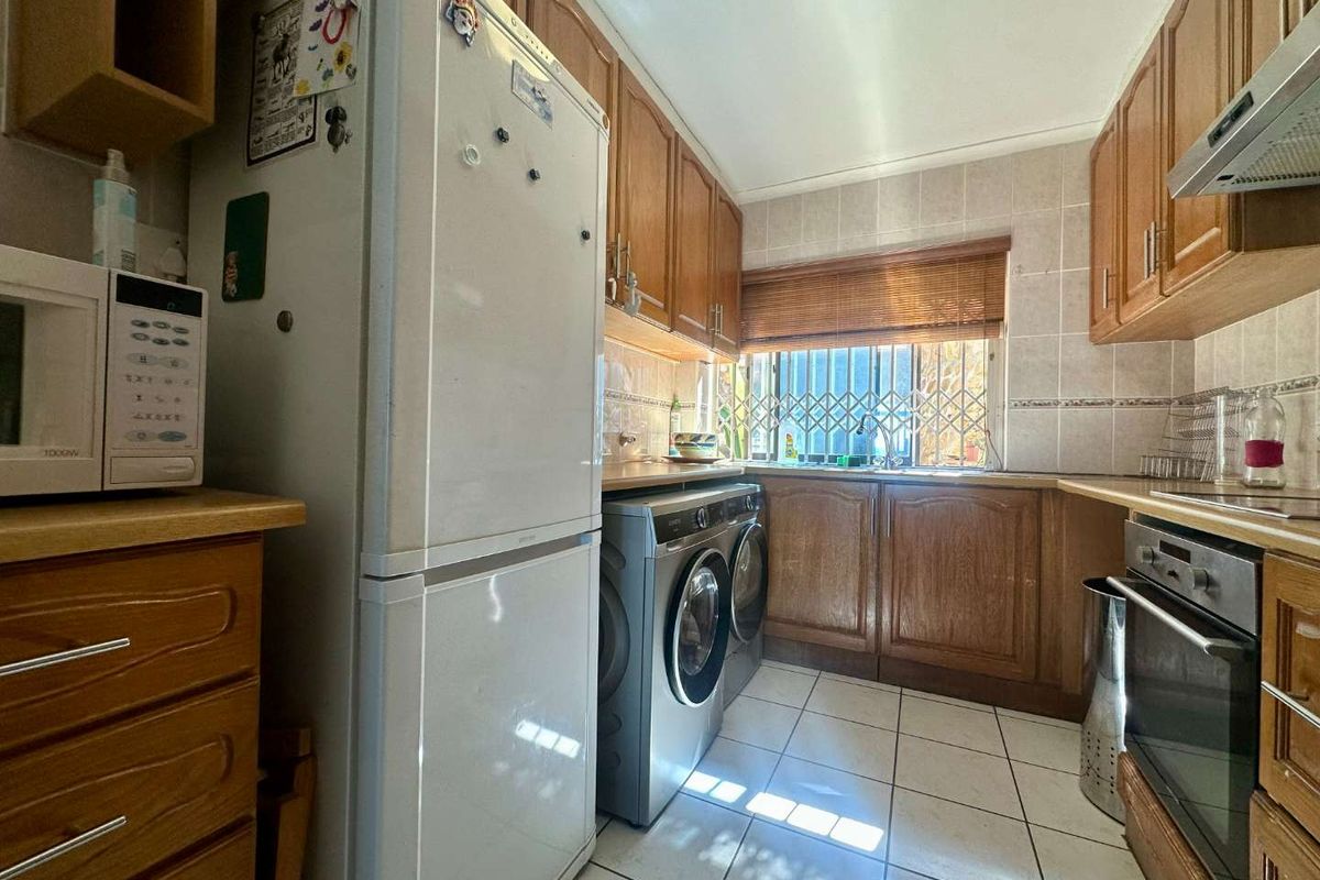 A functional kitchen featuring wooden cabinetry, tiled splashbacks, tiled flooring, and integrated oven and extractor fan.