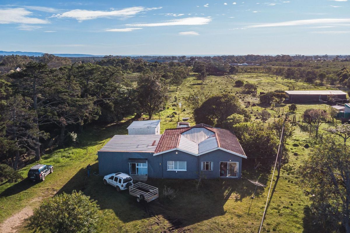 Aerial view of a small holding property featuring a main dwelling with a mixed metal and tiled roof, surrounded by expansive rural grounds.