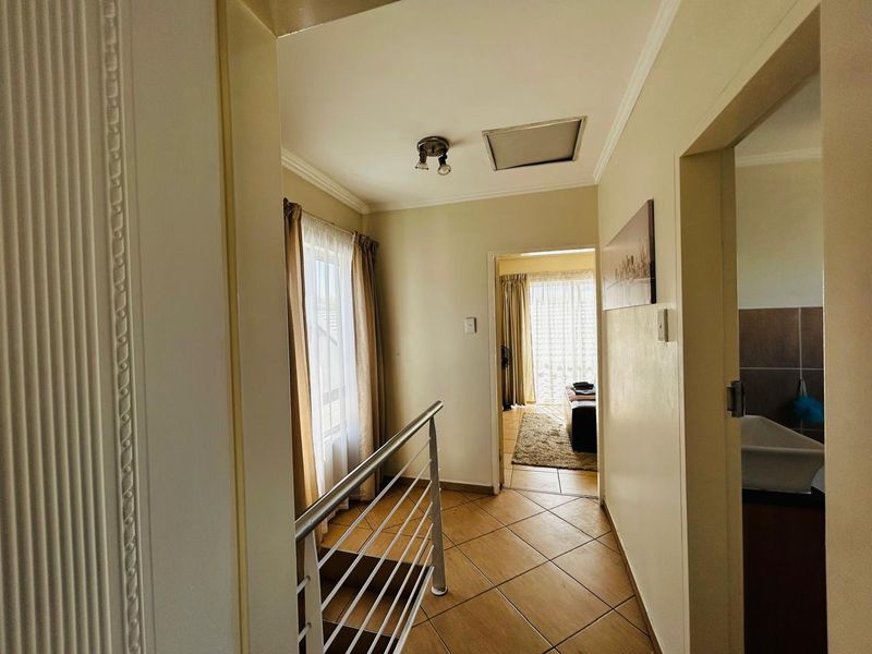 A bright hallway featuring tiled flooring and a metal balustrade, providing access to adjacent rooms and a staircase.