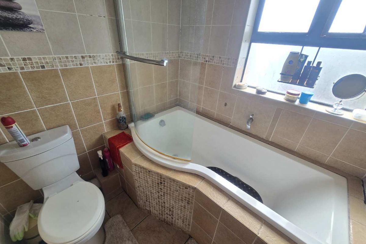 A functional bathroom featuring a tiled bathtub with a glass shower screen, a standard toilet, and neutral wall and floor tiling.