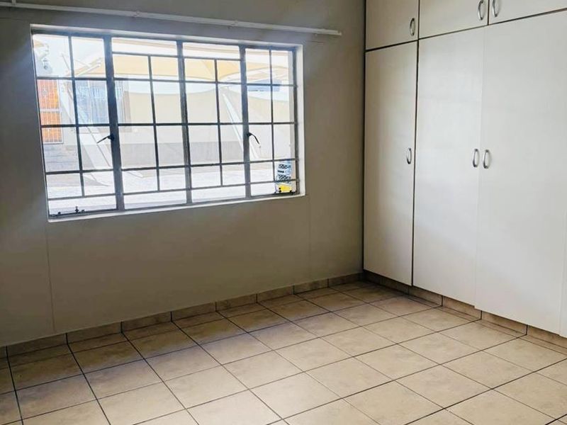 A clean, empty bedroom featuring neutral tiled flooring, built-in storage cupboards, and a window fitted with security bars.