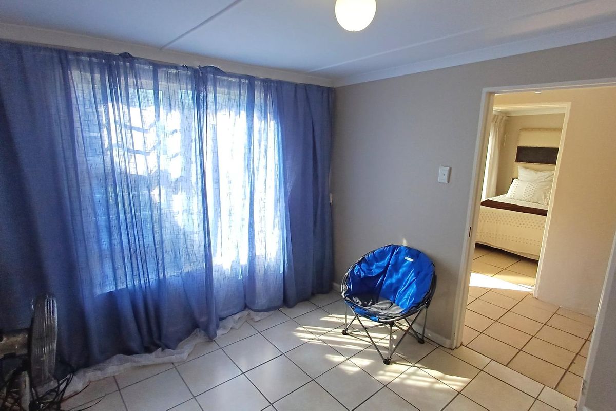 A bright, tiled living area featuring coved ceilings and a doorway leading to an adjacent bedroom.