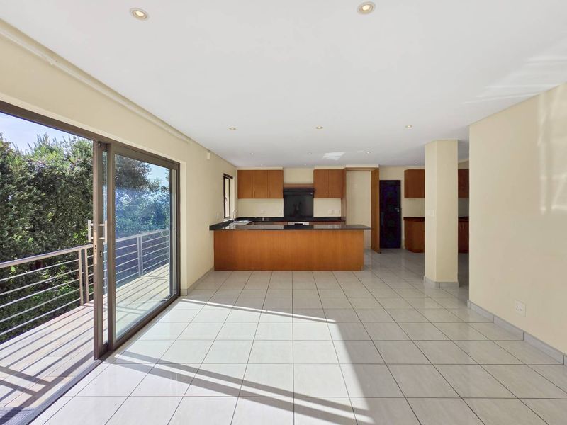 Spacious open-plan kitchen and living area featuring tiled floors, built-in wooden cabinetry, granite countertops, and large sliding doors leading to an outdoor balcony.