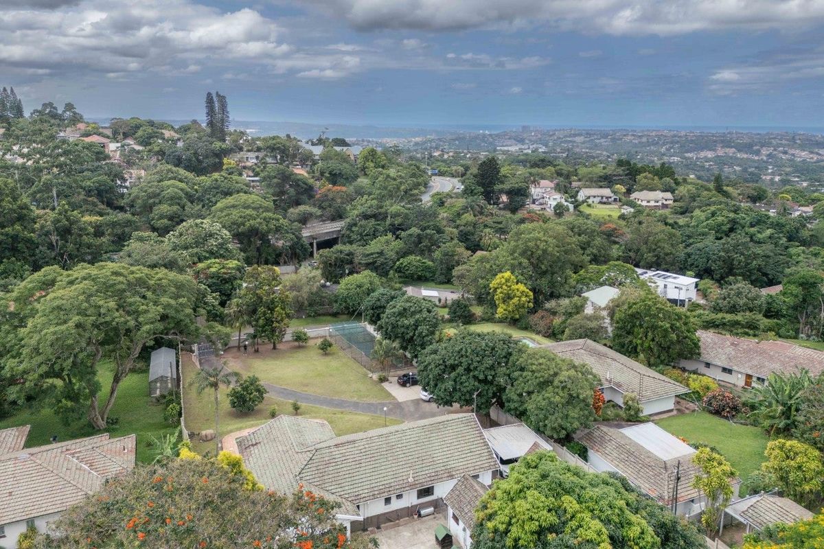 Aerial view of a residential property featuring a tennis court, tiled roof structures, and expansive landscaped grounds within a suburban neighborhood.
