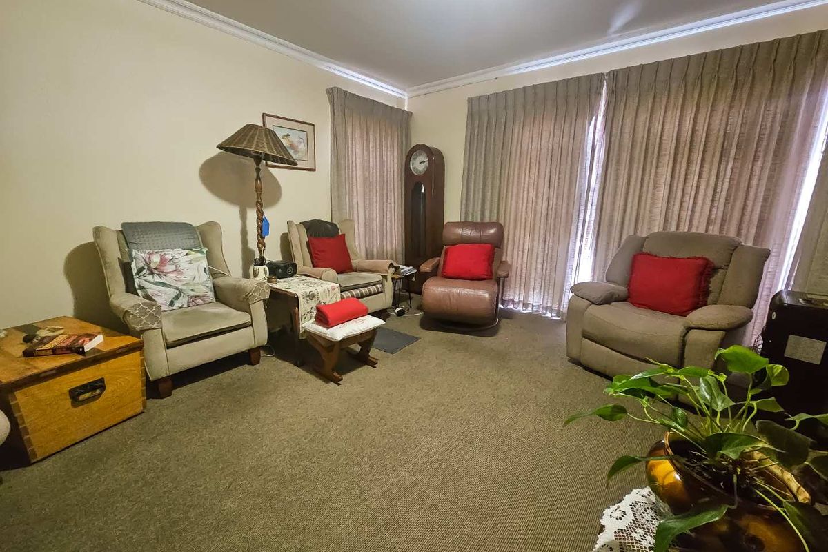 A comfortable living room featuring wall-to-wall carpeting, crown molding, and large windows covered by floor-to-ceiling curtains.