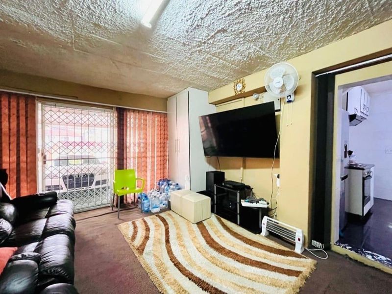 Living room featuring textured ceiling, built-in wardrobe, and security gate access to the exterior. The space requires cosmetic updates to improve overall condition.