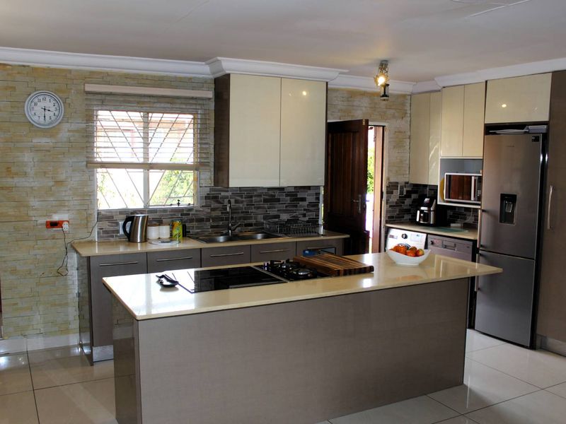 Modern kitchen featuring a central island with integrated hob, stone tile feature wall, sleek cabinetry, and high-quality built-in appliances.