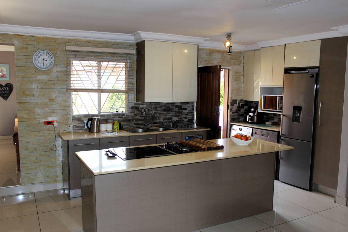Modern kitchen featuring a central island with integrated hob, stone tile feature wall, sleek cabinetry, and high-quality built-in appliances.