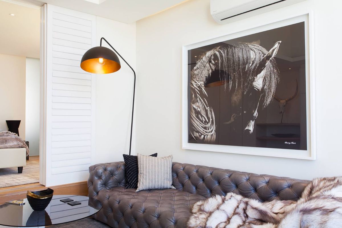 A well-appointed living room featuring a wall-mounted air conditioning unit and white shutter doors leading to an adjacent bedroom.
