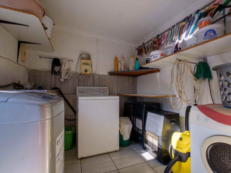A functional laundry room featuring tiled flooring, wall-mounted shelving, and tiled splashback areas for utility use.