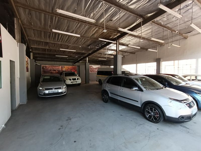Spacious industrial garage area featuring exposed steel roof trusses, concrete flooring, and overhead fluorescent lighting, suitable for vehicle storage or workshop use.
