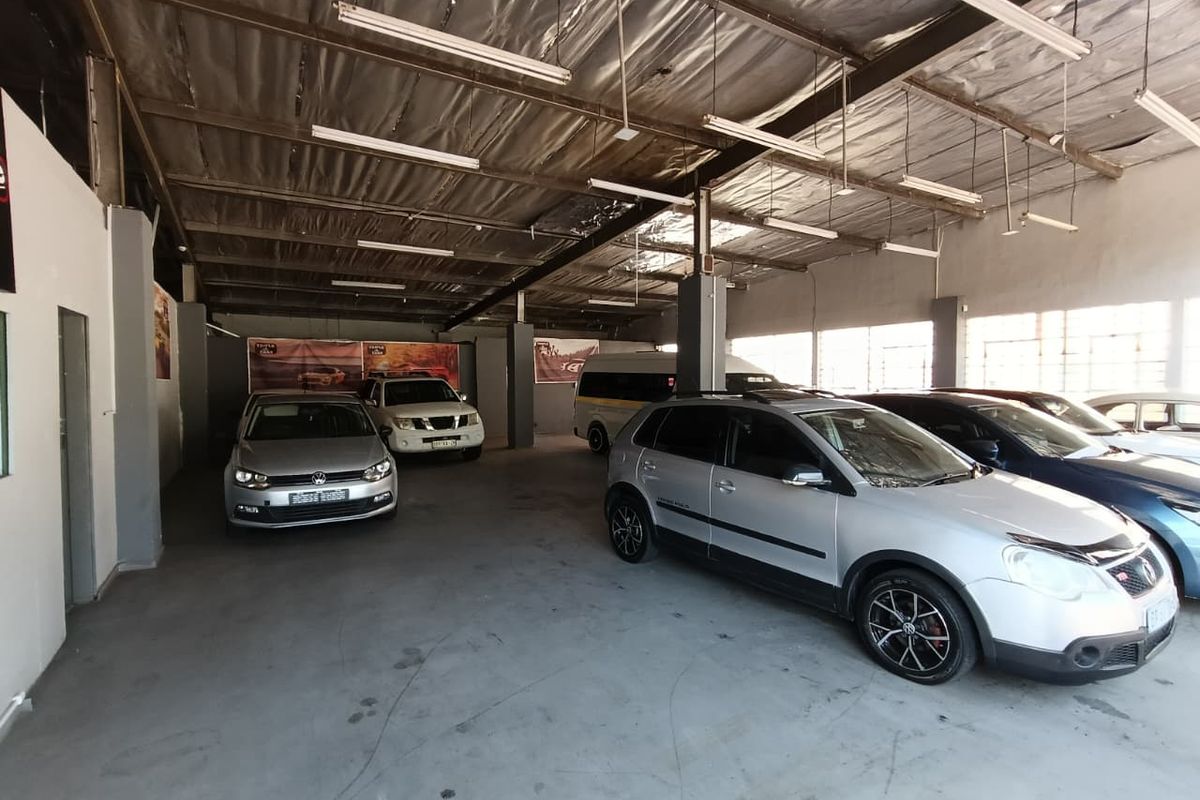 Spacious industrial garage area featuring exposed steel roof trusses, concrete flooring, and overhead fluorescent lighting, suitable for vehicle storage or workshop use.