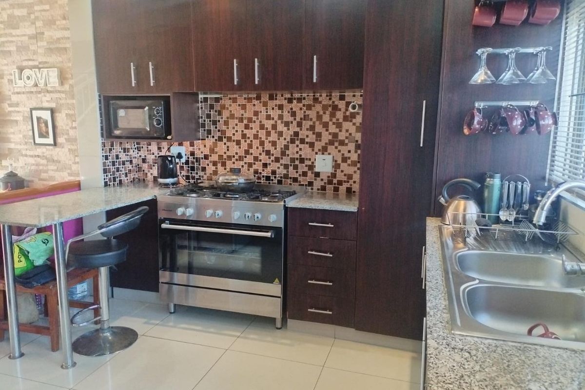 Modern kitchen featuring dark wood cabinetry, granite countertops, mosaic tile backsplash, and a stainless steel gas stove with a breakfast bar.