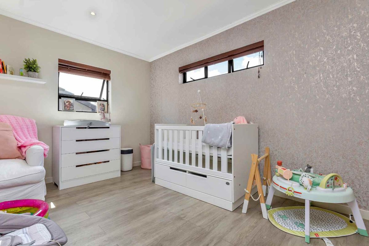 A well-maintained bedroom featuring light wood-look flooring, a textured feature wall, and horizontal windows with fitted blinds.