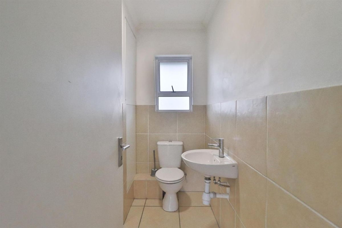 A compact guest bathroom featuring a wall-mounted basin, a standard toilet, and neutral wall tiling.