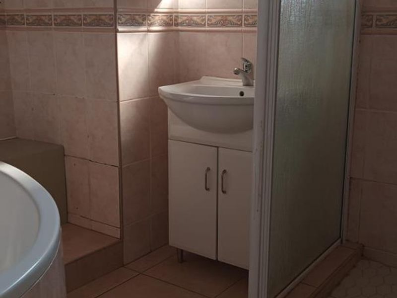 A functional bathroom featuring a corner bathtub, separate shower enclosure, and a vanity basin with integrated storage, finished with neutral wall and floor tiling.