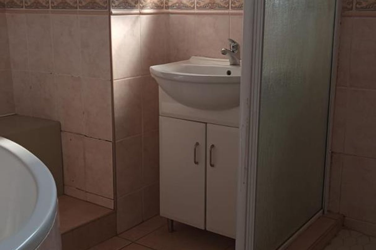 A functional bathroom featuring a corner bathtub, separate shower enclosure, and a vanity basin with integrated storage, finished with neutral wall and floor tiling.