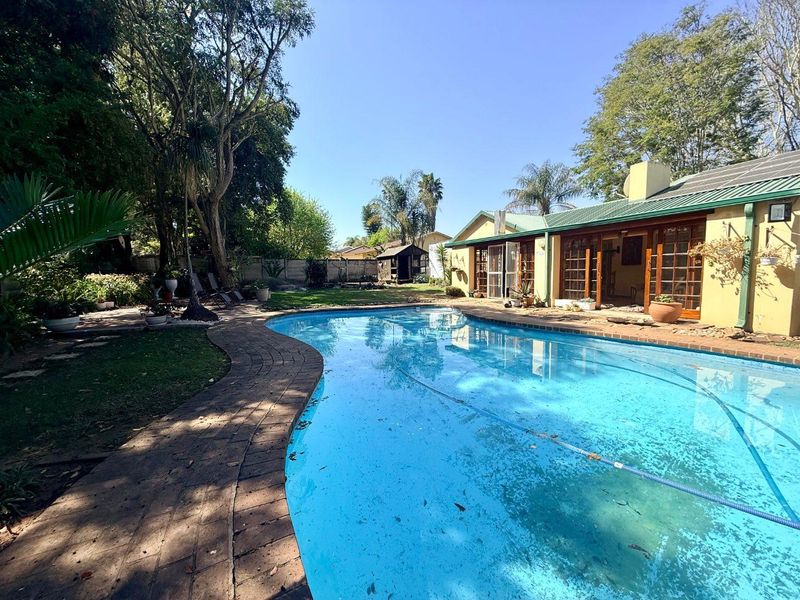 A spacious backyard featuring a swimming pool with brick paving, mature trees, and direct access to the home through timber-framed doors.