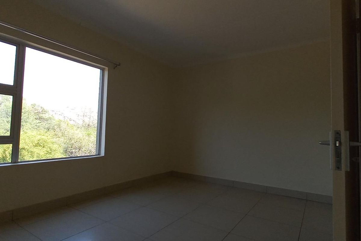 An empty bedroom featuring tiled flooring and a large window with natural light, providing a blank canvas for interior design.
