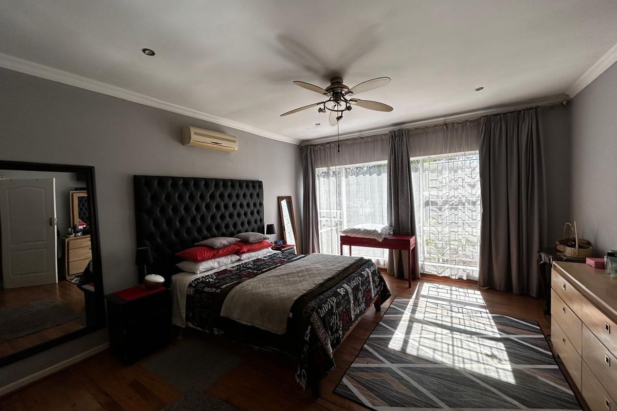 Spacious bedroom featuring laminate flooring, a ceiling fan, wall-mounted air conditioning, and large sliding glass doors providing natural light and access to the exterior.