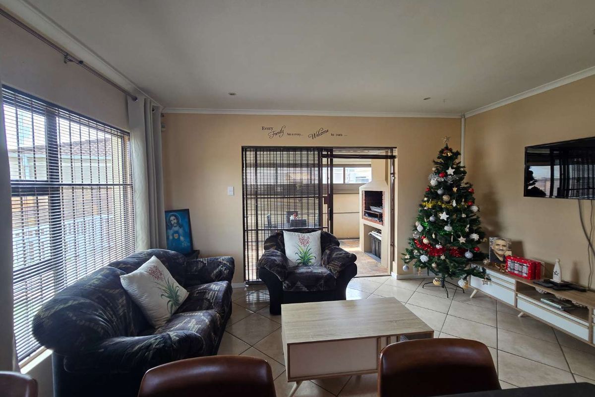 Spacious living room featuring large windows, tiled flooring, and direct access to a covered patio area with a built-in braai.