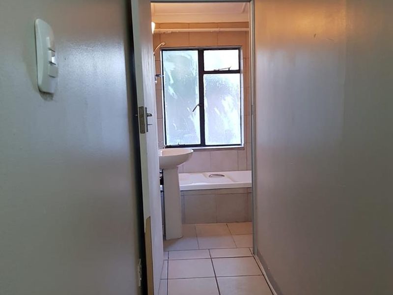 A view through a hallway leading into a bathroom featuring a pedestal basin and a built-in bathtub with tiled flooring.