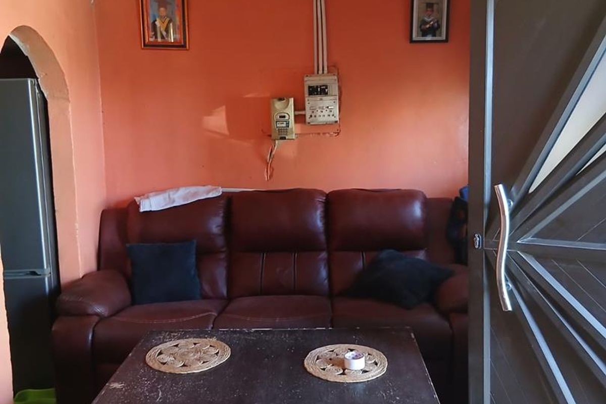 A living room area featuring tiled flooring, exposed electrical conduit, and a decorative entrance door.