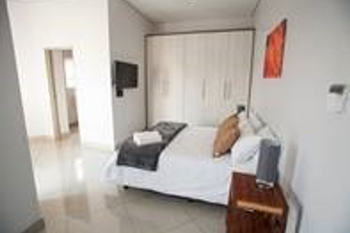 A well-lit bedroom featuring neutral tiled flooring and ample built-in cupboard storage space.