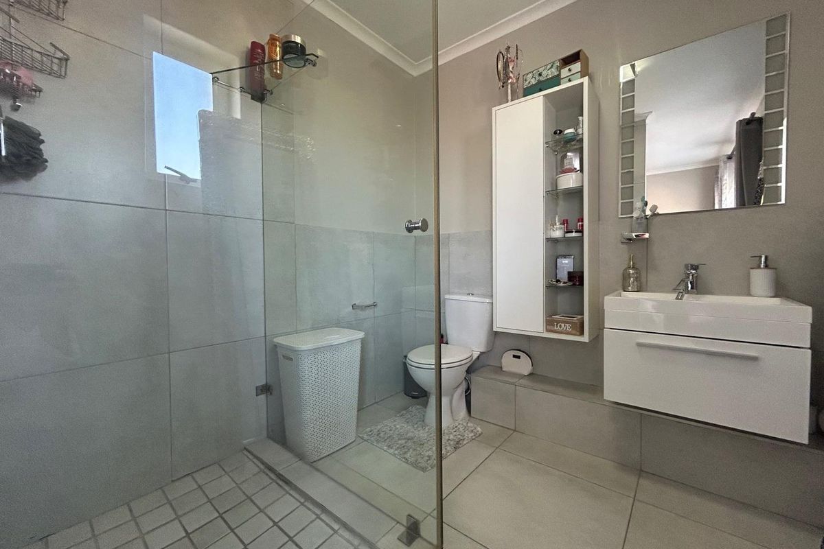 Modern bathroom featuring a glass-enclosed walk-in shower, wall-mounted vanity with basin, and a built-in storage cabinet.