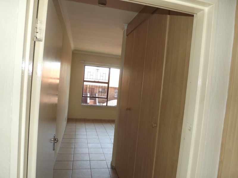 An empty bedroom featuring tiled flooring, built-in wooden cupboards, and a window with security bars, offering a functional and neutral living space.