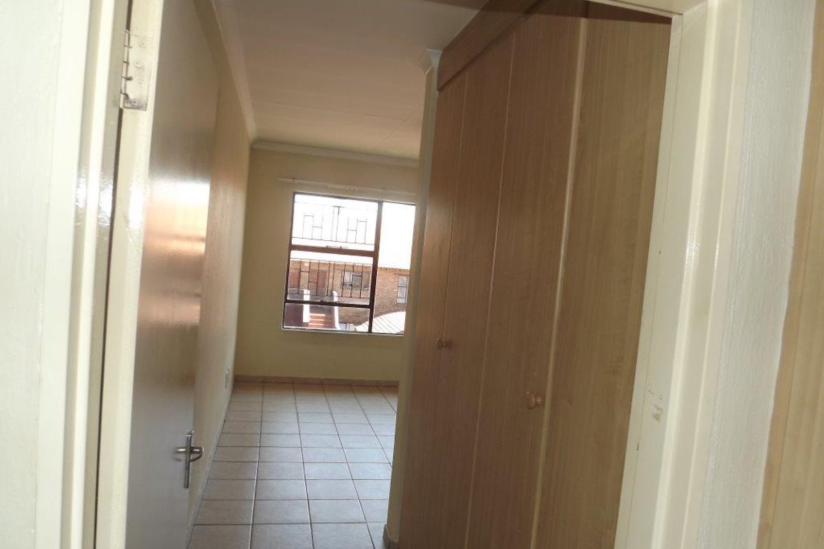 An empty bedroom featuring tiled flooring, built-in wooden cupboards, and a window with security bars, offering a functional and neutral living space.