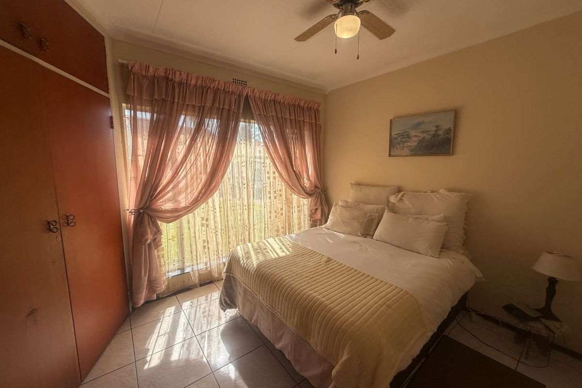 A bedroom featuring tiled flooring, a built-in wardrobe, and a ceiling fan, with natural light entering through a window with security bars.