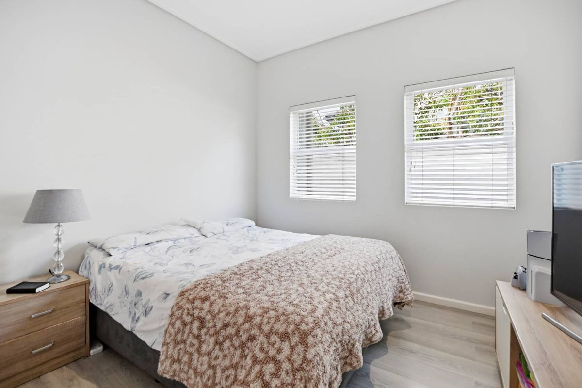 A bright and well-maintained bedroom featuring neutral walls, laminate flooring, and dual windows fitted with venetian blinds.