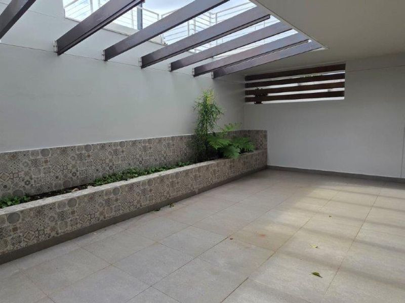 A spacious covered patio featuring a modern pergola, tiled flooring, and a built-in decorative planter box, offering a clean and versatile outdoor living space.