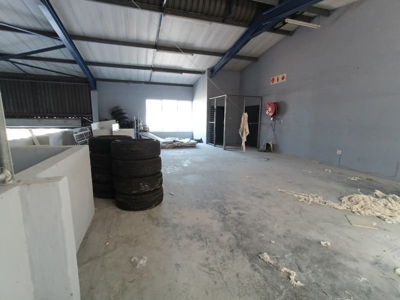 Spacious industrial utility area featuring exposed steel roof trusses, concrete flooring, and a built-in metal security cage, suitable for storage or workshop use.