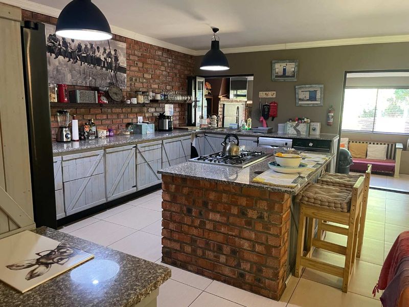 Spacious kitchen featuring an exposed brick feature wall, granite countertops, a central island with a gas hob, and ample built-in cabinetry.