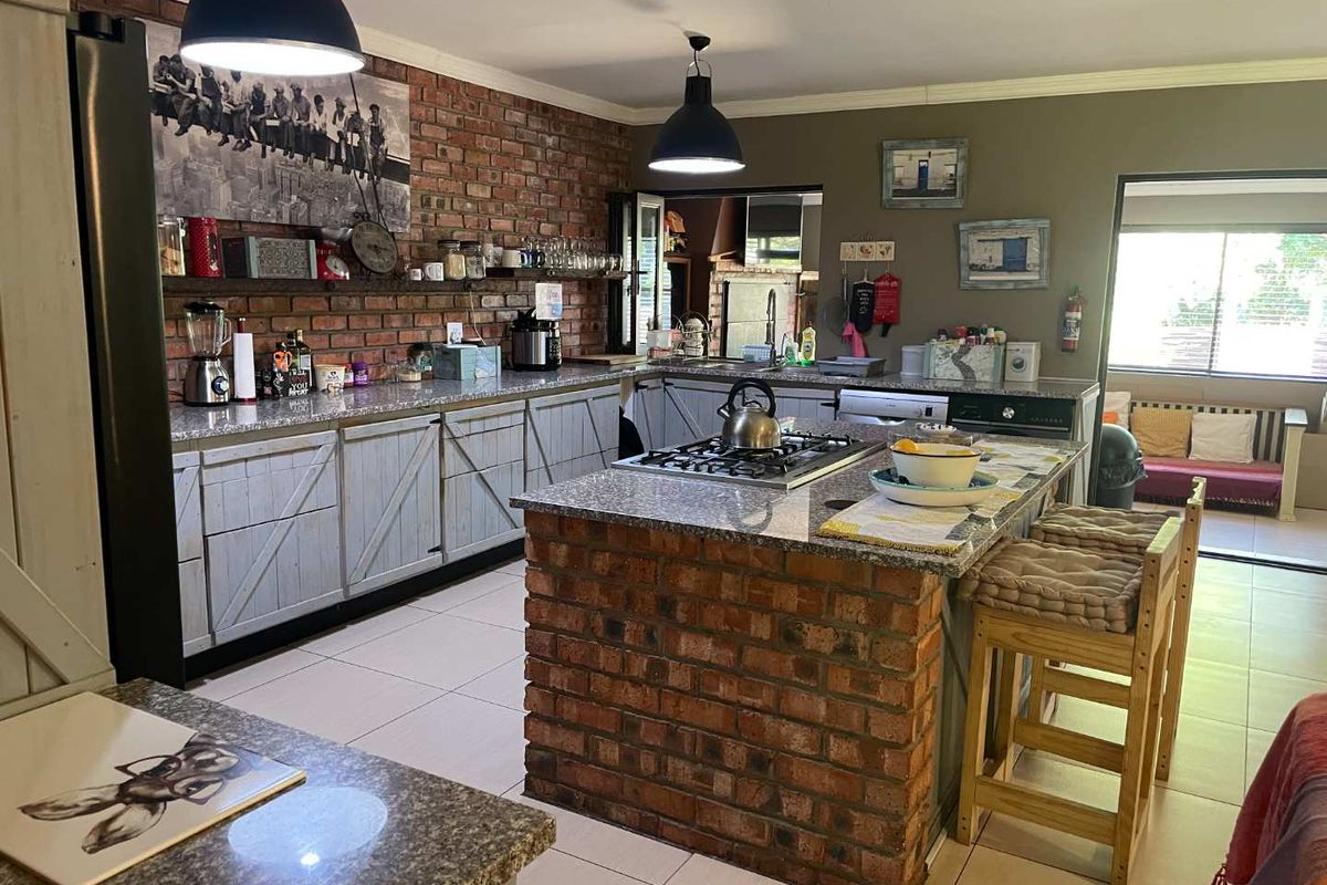 Spacious kitchen featuring an exposed brick feature wall, granite countertops, a central island with a gas hob, and ample built-in cabinetry.