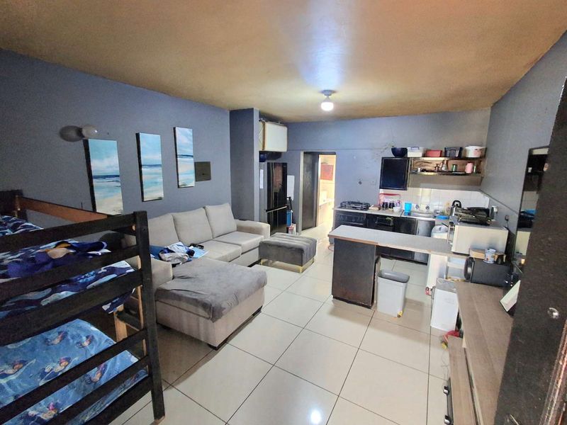 Open-plan living area featuring a combined kitchen with built-in cabinetry, stove, and breakfast counter, finished with tiled flooring throughout.