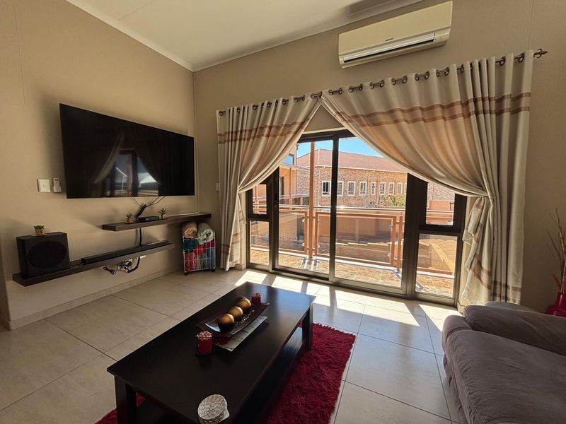A well-maintained living room featuring tiled flooring, a wall-mounted air conditioning unit, and large sliding glass doors providing access to an outdoor balcony.