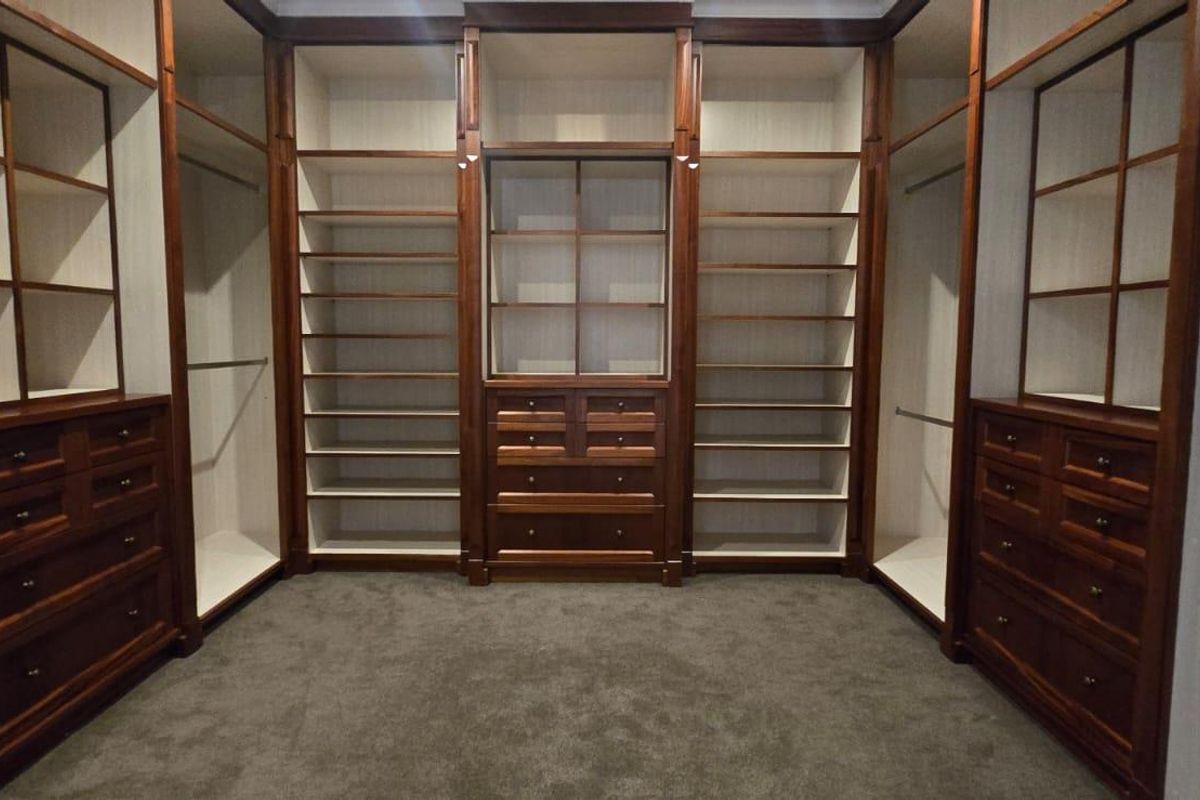 A spacious walk-in closet featuring extensive custom-built wooden cabinetry, including integrated shelving, hanging rails, and multiple storage drawers.