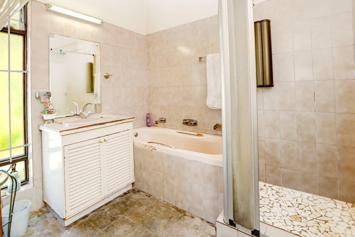 A dated bathroom featuring a built-in bathtub, separate shower enclosure, and vanity unit with integrated basin, requiring cosmetic updates and floor restoration.