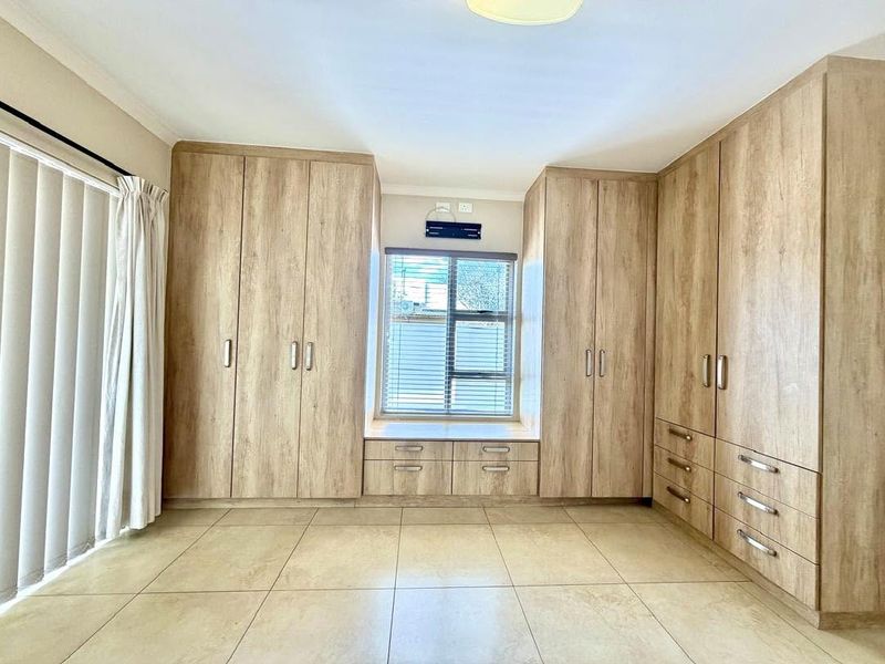 A spacious bedroom featuring extensive light wood-finish built-in cabinetry, a window seat, and neutral tiled flooring.