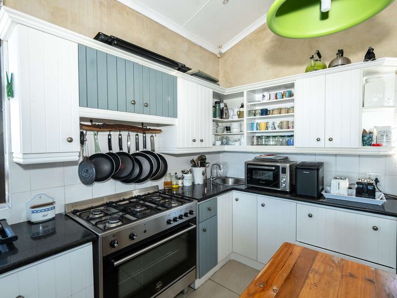 A functional kitchen featuring white and blue cabinetry, granite countertops, a gas stove with oven, and a vaulted ceiling with tiled backsplash.