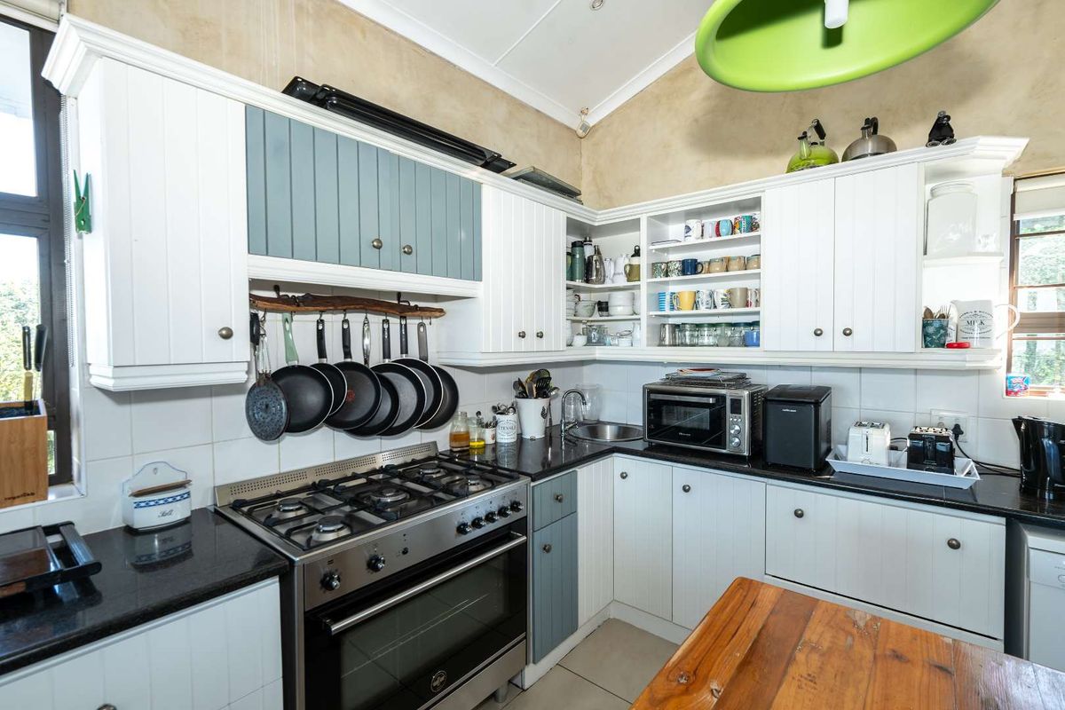 A functional kitchen featuring white and blue cabinetry, granite countertops, a gas stove with oven, and a vaulted ceiling with tiled backsplash.
