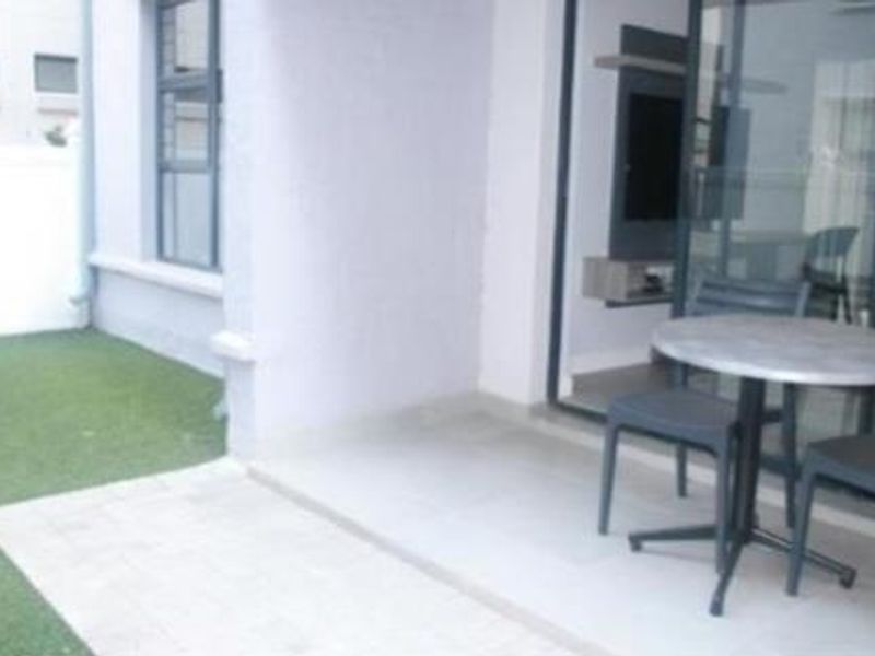 A covered patio area featuring tiled flooring and direct access to a small private garden space with artificial grass.