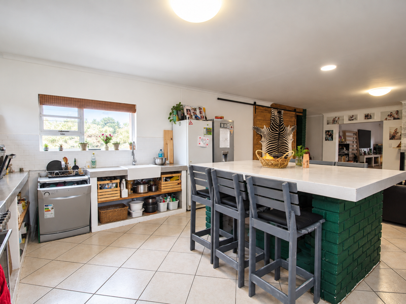 Open-plan kitchen featuring a large island with a brick base, farmhouse sink, and tiled flooring, seamlessly connecting to the adjacent living area.