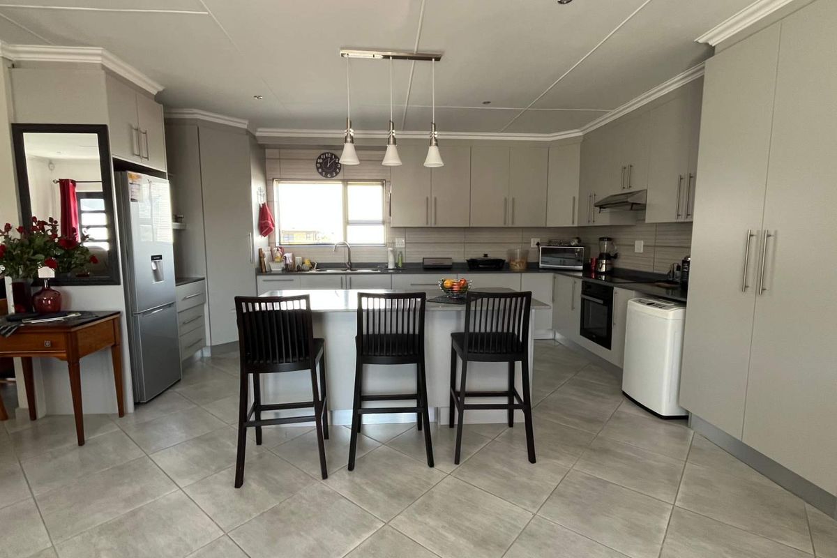 Modern kitchen featuring light grey cabinetry, a central island with breakfast bar seating, tiled flooring, and integrated appliances.