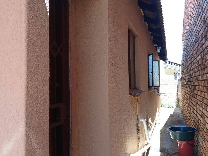 A narrow side passage of the house featuring plastered walls, tiled roof eaves, and security gate access.