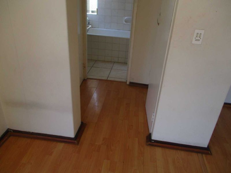 A view from a hallway looking into a bathroom, featuring laminate flooring and plain walls in need of maintenance.