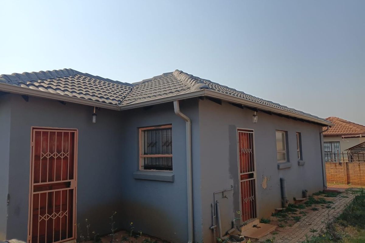 Rear exterior view of the house featuring a tiled roof, security gates on doors, and paved pathways with visible exterior wall maintenance required.